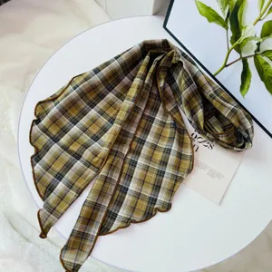 Detailed shot of a vintage plaid ribbon scarf with lettuce edge on a white tabletop.
