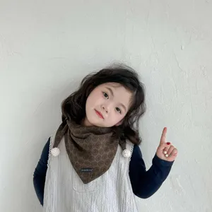 Toddler brown printed triangular scarf close-up, warm neck warmer with cute pom-poms.
