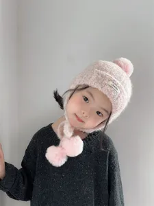 Vue détaillée du bonnet en tricot rose pour enfants avec protège-oreilles et pompons chauds.