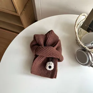 Close-up detail view of brown kids knitted scarf with cute bear patch on white table.