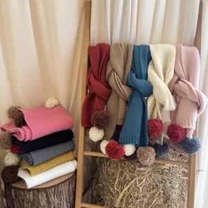 Vue de détail d'écharpes tricotées colorées pour enfants avec pompons doux sur une échelle.