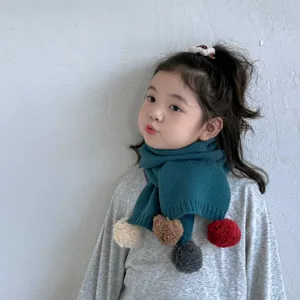 Vue rapprochée de l'écharpe en tricot pour enfants avec des accents de pompons en peluche colorés.