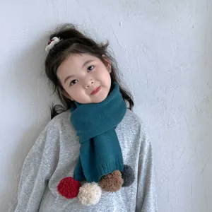 Gros plan sur l'écharpe en tricot pour enfants vert foncé avec des pompons colorés et doux.