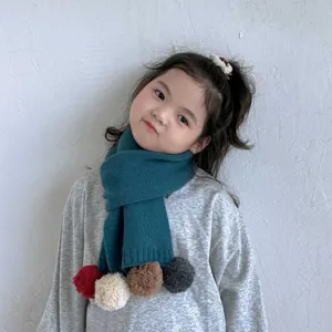 Gros plan détail d'écharpe tricotée pour enfants avec pompons colorés portée par un enfant.