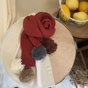 Vue détaillée de l'écharpe d'hiver rouge et douillette pour enfants avec des pompons colorés.