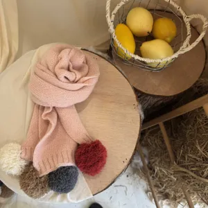 Détail écharpe en tricot rose pour enfants avec pompons colorés pour un look chaud et chic.