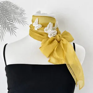 Dettaglio foulard in chiffon, elegante nastro giallo con farfalle in pizzo bianco, accessorio chic.
