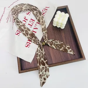 Detailed shot of retro leopard print neck scarf with bead accent, styled on wooden tray.