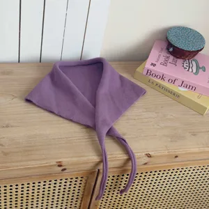 Detail shot of a purple knitted triangular scarf with thin ties, displayed on a wooden table.
