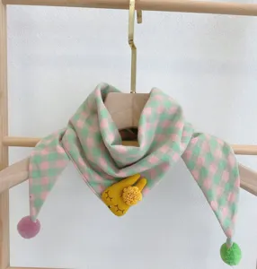 Close-up detail of baby cotton plaid scarf featuring cute yellow rabbit doll and pom-poms.