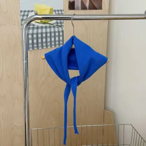 Close up view of a vibrant blue knitted triangular scarf with long straps hanging on a hanger.