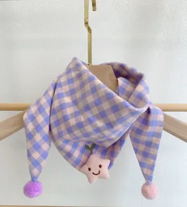 Close-up details of cute baby checkered scarf featuring a plush star toy and lovely pom-poms.