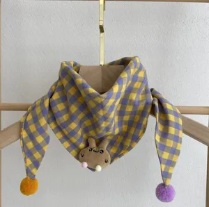 Close-up of cute baby cotton plaid scarf featuring cartoon rabbit plush and cute pom poms.