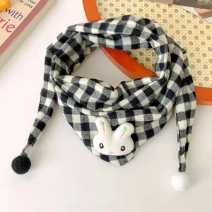 Close-up detail of black and white plaid baby scarf with cute rabbit doll and pom-pom ends