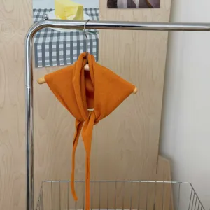 Detail shot of orange knitted triangular scarf with tie strings hanging on wooden hanger.