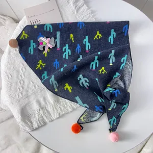 Detail shot of a baby triangular scarf with colorful cactus print and cute pom-poms.