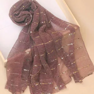 Close-up detail of shimmering pleated scarf with metallic gold square dots on soft fabric.