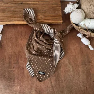 Detail view of a brown polka dot and striped children's scarf with brand tag on rustic wood table.