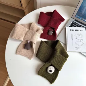 Vista detallada de bufandas cruzadas de punto para niños con adorables dijes de peluche.