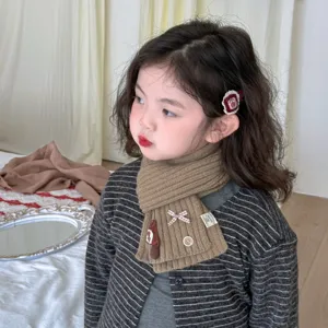 Detailed shot of kids brown knitted scarf with cute bow and mushroom decoration worn by a child model.
