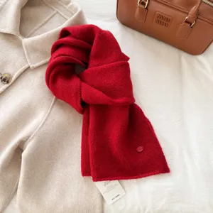 Close-up detail view of a soft red knitted scarf with a textured fabric and attached brand tag.