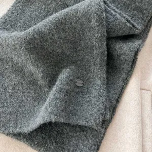 Dark grey knitted scarf detail shot, showing soft woolen texture and metal brand tag.