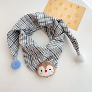 Closeup detail of baby plaid scarf featuring cute animal plush decor and soft pom-poms.
