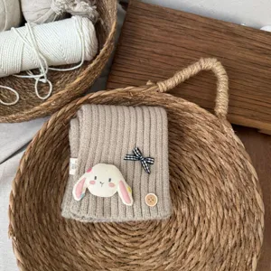 Detailed view of the cute knitted kids scarf featuring a plush rabbit patch and plaid bow.