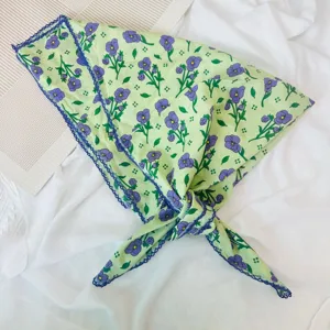 Close-up detail of a light green cotton floral square scarf with purple blooms and blue lace trim.