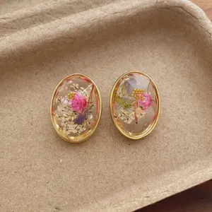 Detail shot of oval resin earrings featuring natural dried flowers and elegant gold metal rims.