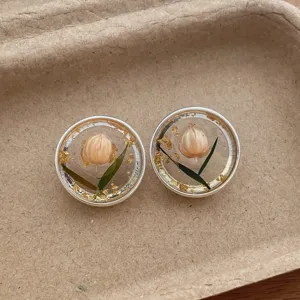 Close-up detail of clear resin stud earrings featuring embedded dry flower buds and gold foil.
