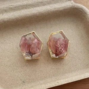 Close-up of geometric transparent resin earrings with pink dried flowers and gold rims.