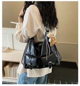 Detail view of the black leather shoulder bag featuring dual front pockets and a cute plush bear.