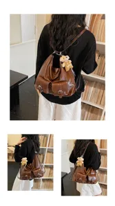 Detailed view of brown leather backpack with front pockets and cute bear pendant accessory.
