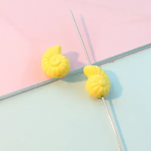 Close-up detail shot of yellow conch shaped acrylic beads on pin for DIY jewelry making accessories.