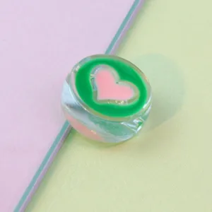Clear detail shot of 21mm transparent round acrylic loose bead with green and pink heart oil design.