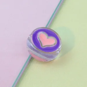 Close-up of transparent round acrylic bead with pink heart pattern for DIY phone charms.