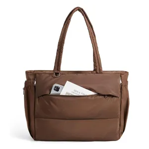 Brown quilted puffer tote bag detail, showing soft padded fabric and front zipper pocket.