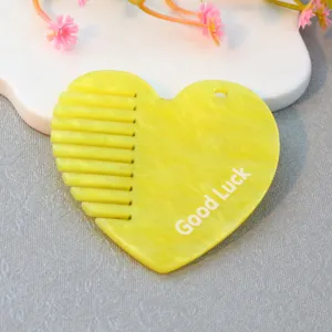 Close-up of yellow acrylic heart-shaped comb detail with hole and Good Luck letter print design.