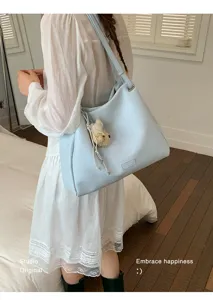 Detail view of the light blue shoulder tote bag with cute bear pendant in indoor setup.