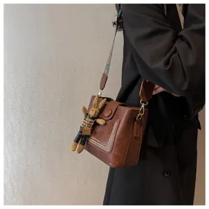 Borsa a secchiello retro in pelle marrone da donna con tracolla larga e simpatico ciondolo.