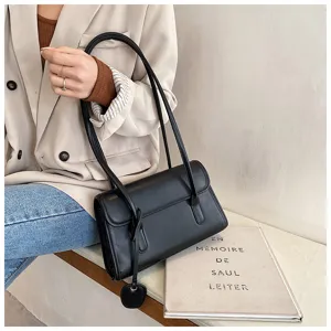 Minimalist black leather shoulder bag detail, elegant underarm style with long strap and charm.