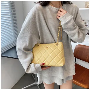 Detailed shot of yellow quilted shoulder bag with chain strap worn by model in casual knit top.