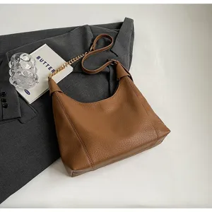 Detailed view of brown litchi pattern leather shoulder bag on gray blazer background.