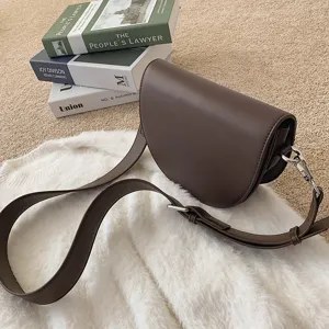 Brown leather saddle bag for women, stylish wide strap crossbody shoulder bag with metal hardware.