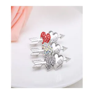 Detailed close-up of sparkling crystal arrow through heart brooches, elegant silver tone design.