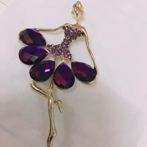 Detailansicht der eleganten goldenen Ballerina-Brosche mit funkelnden lila Strasssteinen.