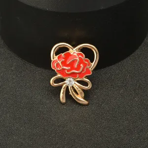 Close-up detail shot of a gold-tone zinc alloy carnation brooch with red enamel and a rhinestone.