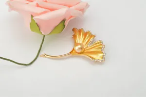 Gold ginkgo leaf brooch detail, featuring shiny rhinestones and a central pearl accent.