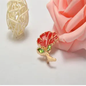 Carnation brooch detail shot, red enamel flower with green crystal leaves, gold plated metal accessory.